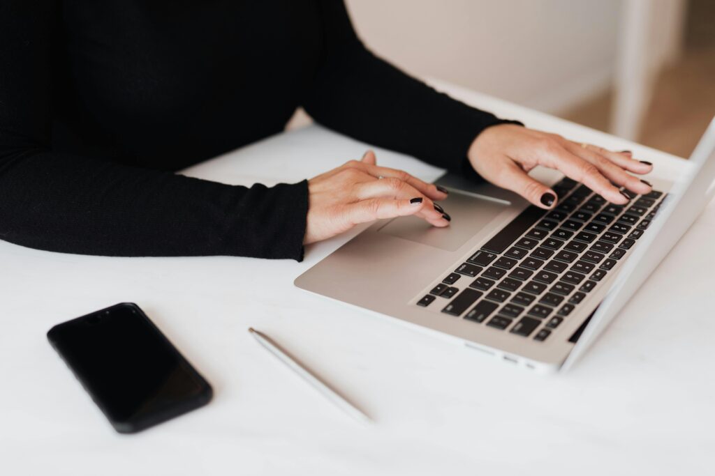 Professional woman typing on a laptop with smartphone and pen on desk, emphasizing modern business lifestyle.