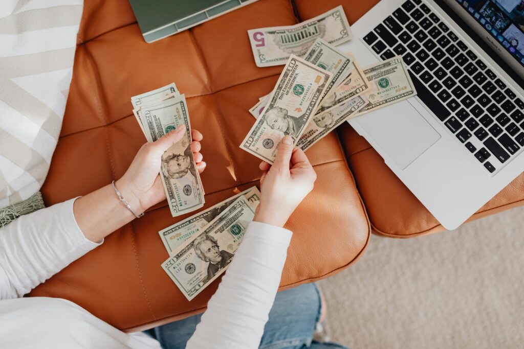 A person counts US dollar bills on a couch with a laptop, symbolizing financial planning.